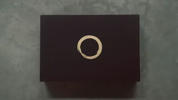 Schwarze Box mit goldenem Kreis auf grauer Fläche.