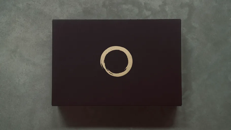 Black box with gold circle on gray surface.