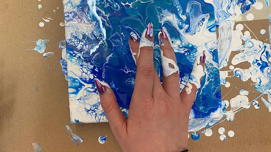Hand paints on canvas with blue swirling patterns.