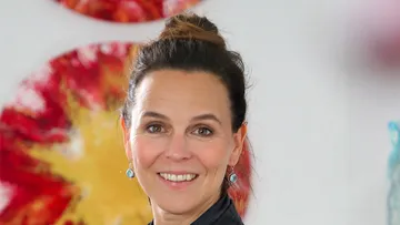Woman smiling in front of colorful artwork.