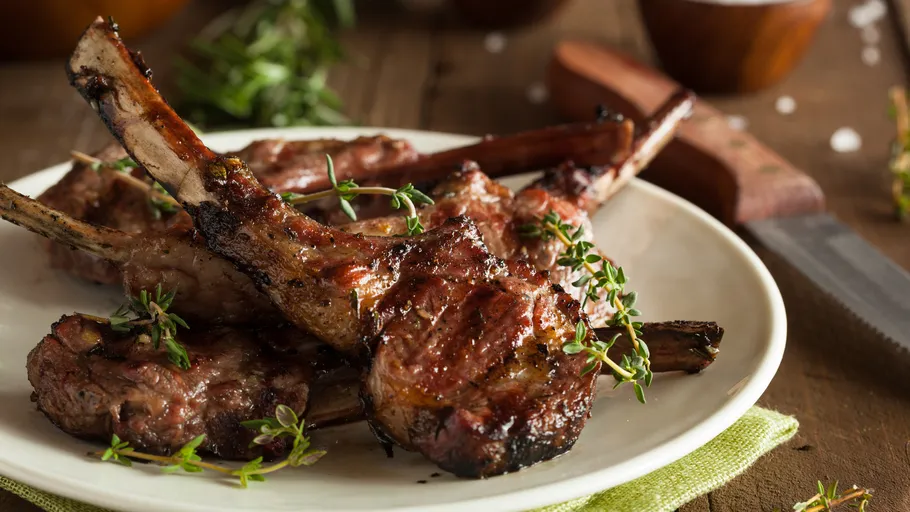 Gegrillte Lammkoteletts auf Teller mit Kräutern.