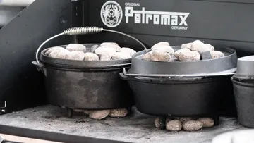 Gusseiserne Töpfe mit Kohle auf Grill.