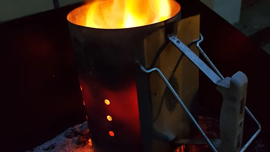 Charcoal chimney starter with flames, nighttime setting.