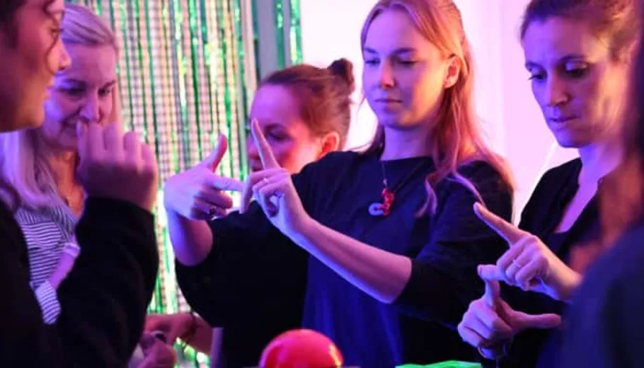 Group of people gesturing indoors, colorful lighting.
