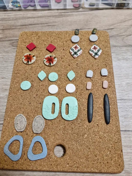 Bunte Harzohrringe auf Korkbrett angeordnet.