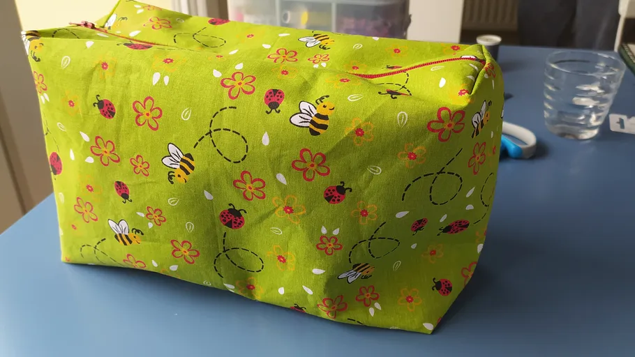 Green fabric bag with bee and flower pattern.