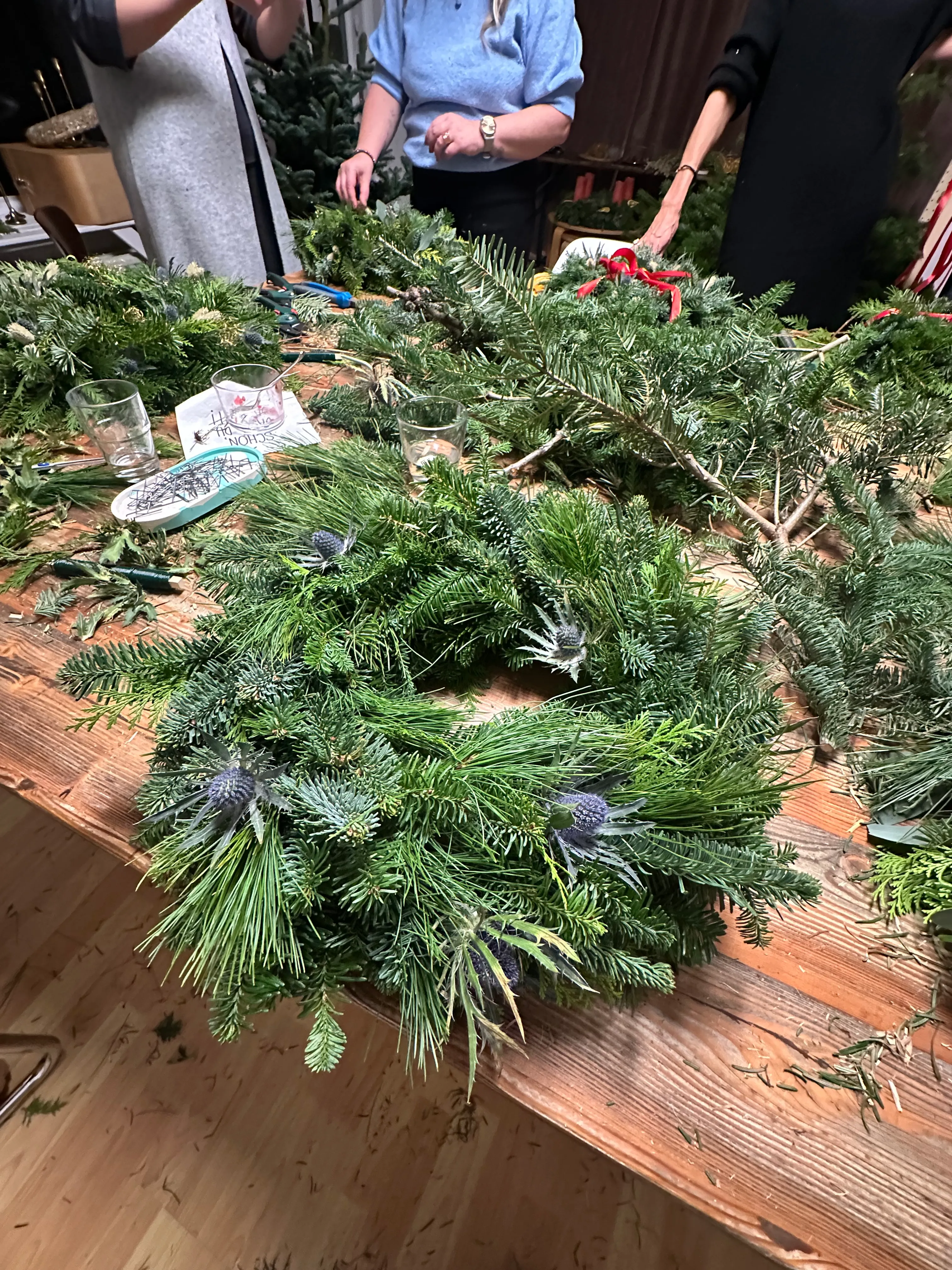 People making wreaths at a wooden table.
