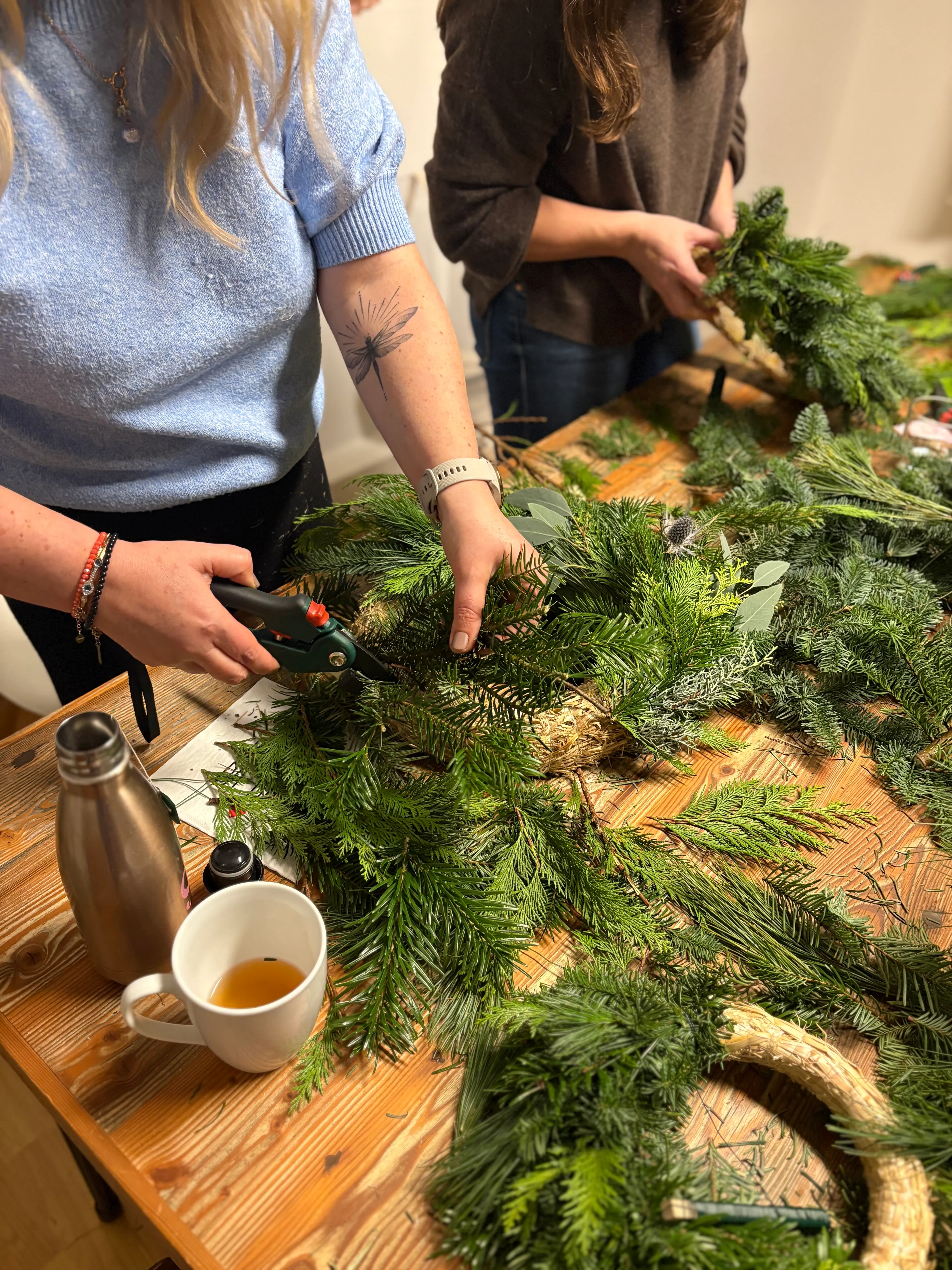 Two people making wreaths on wooden table.