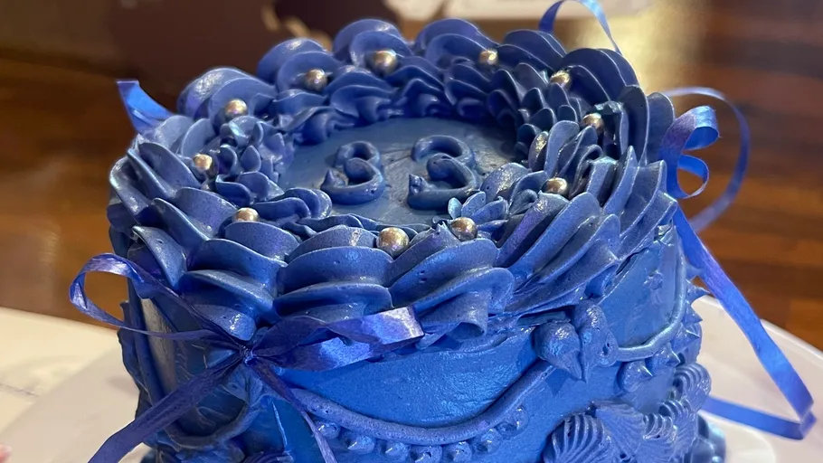 Blue cake with decorative icing and ribbons.