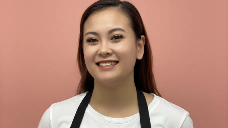 Smiling person wearing apron against pink background.