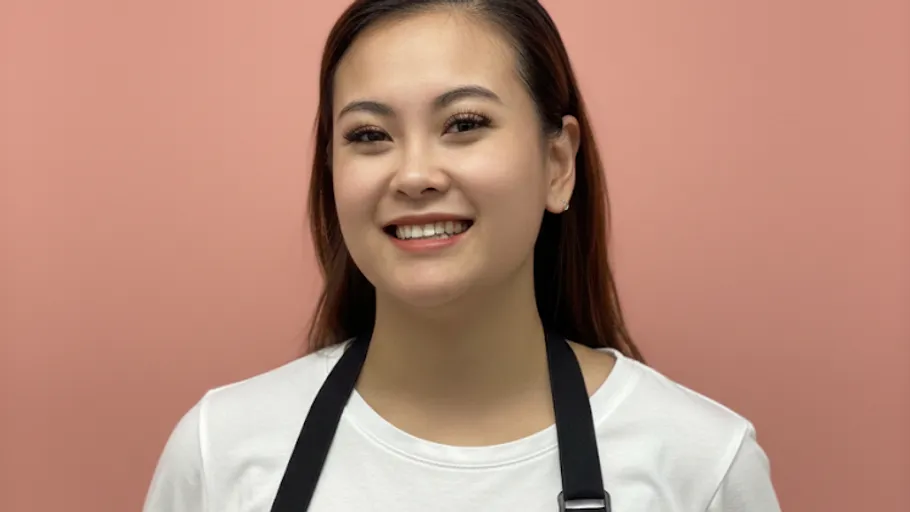 Smiling person wearing apron, pink background.