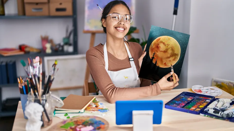 Artist smiling, holding moon painting, art studio.