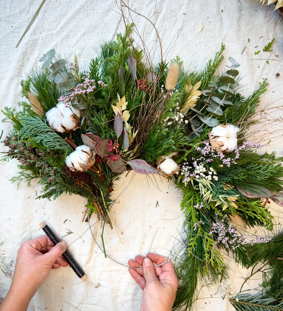 Hands arranging floral wreath on fabric surface.