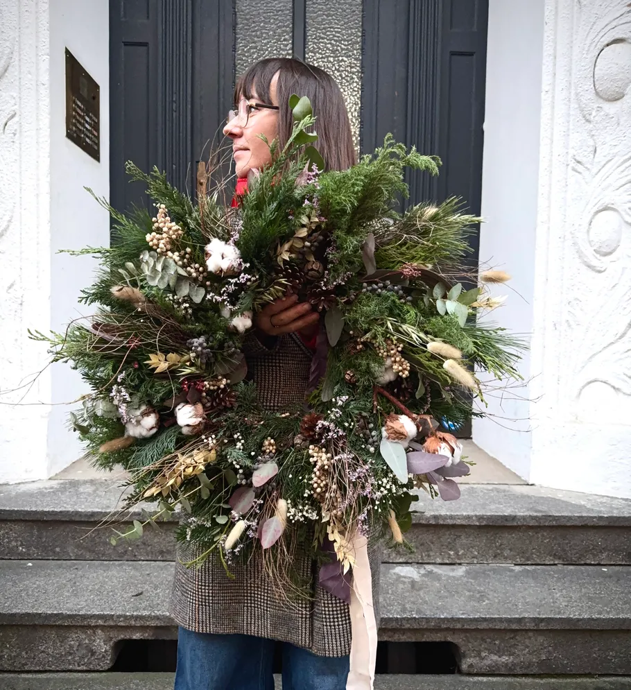 Person holding a large decorative wreath outdoors.