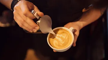 Barista creating latte art in cup.