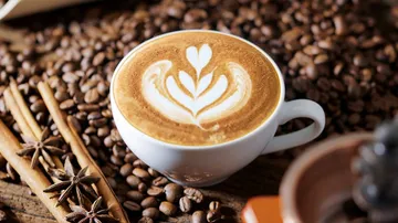 Lattekunst in Tasse von Kaffeebohnen umgeben.