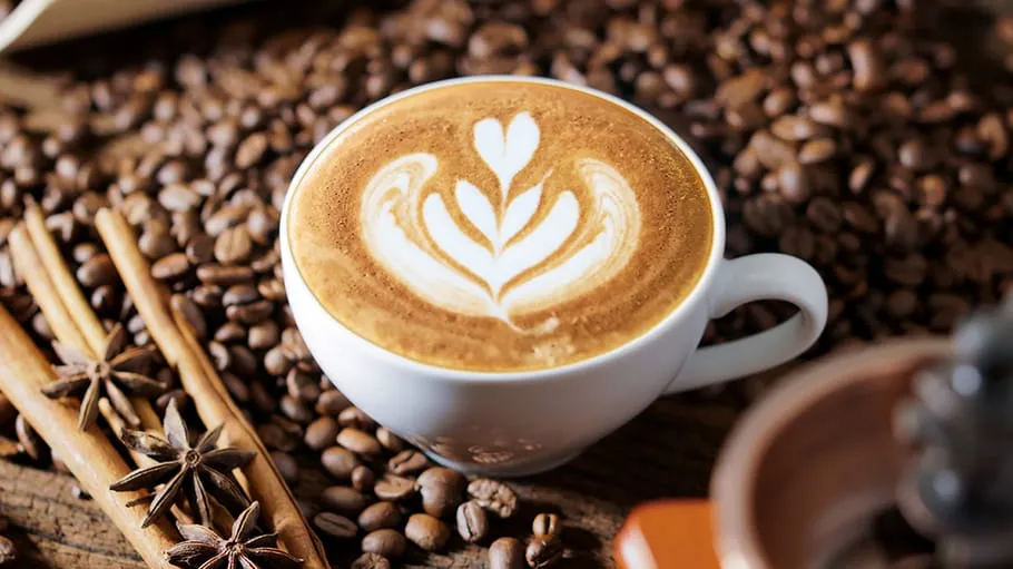 Lattekunst in Tasse von Kaffeebohnen umgeben.