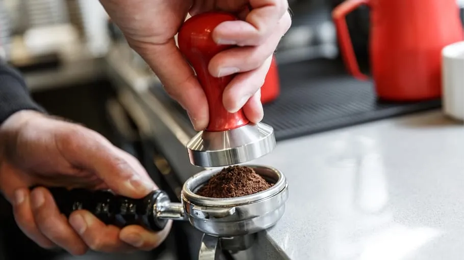 Hand pressing coffee grounds with tamper, kitchen counter.
