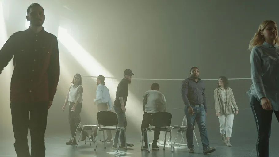 People walk past chairs in a dim room.