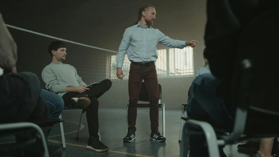 Man standing, gesturing, seated group around.