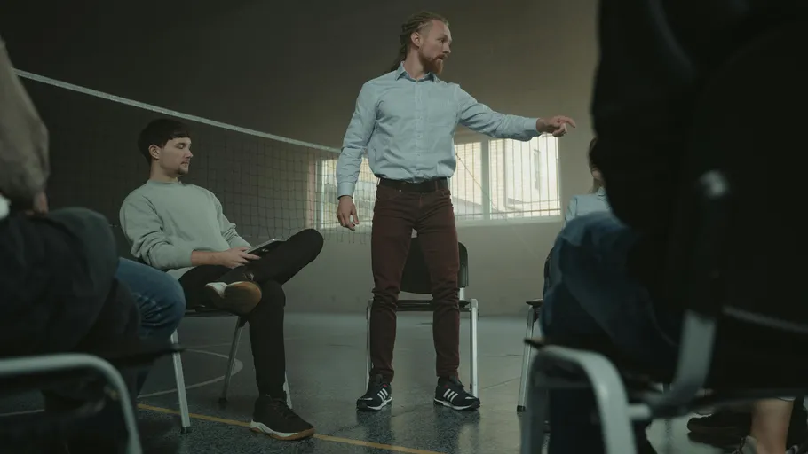 Man standing, speaking to seated group indoors.