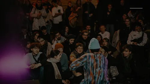 Performer addresses seated audience at night event.