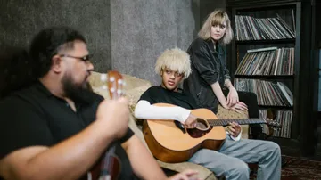 Drei Personen spielen Gitarre in einem Raum.