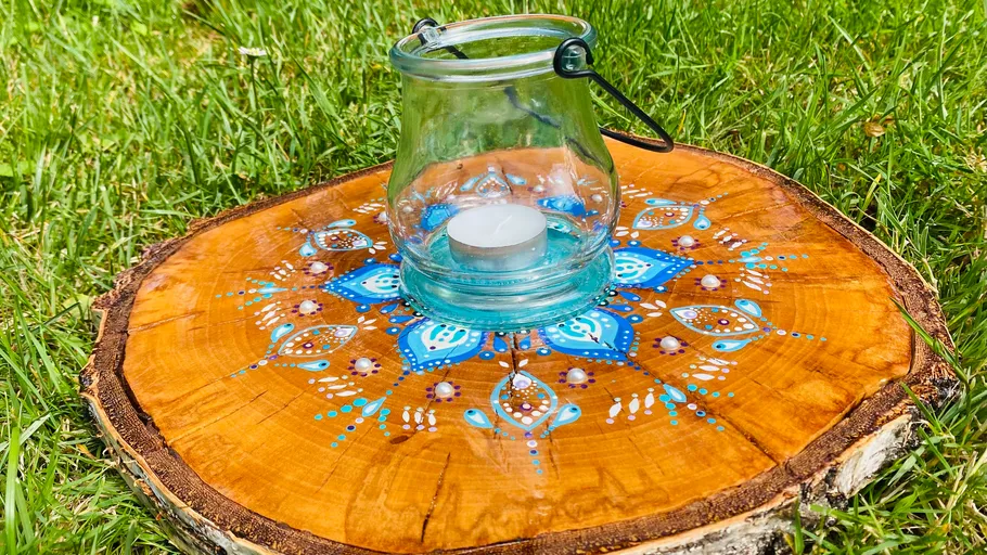 Painted wood slice with candleholder on grass.
