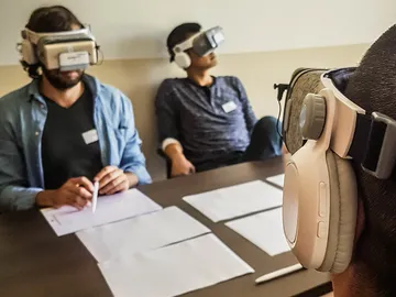 Three people are wearing VR headsets and are sitting at the table.
