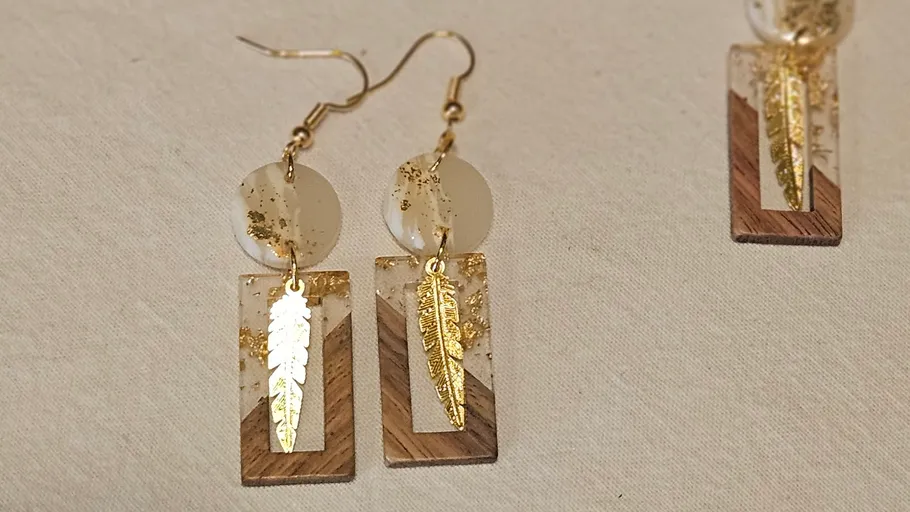 Gold feather earrings on white background.