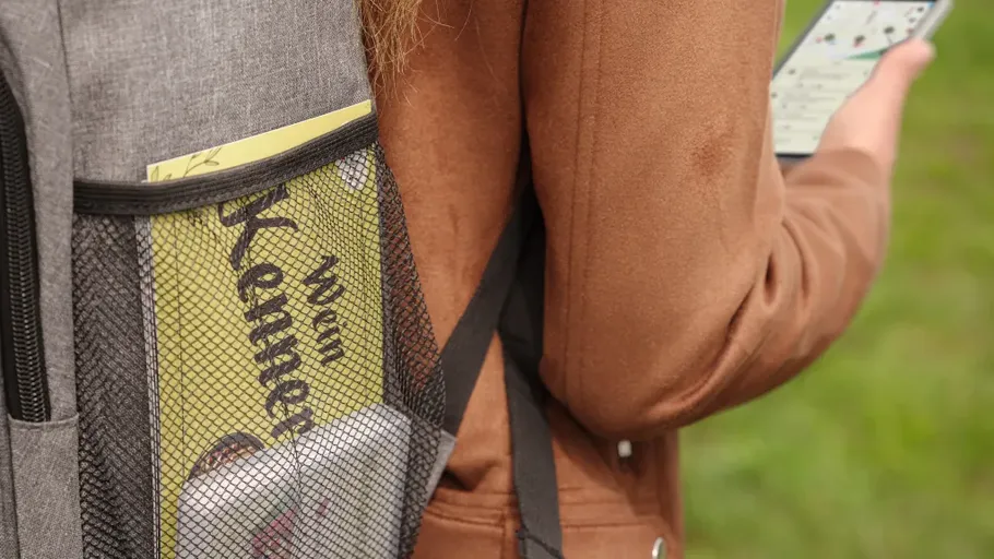 Person holding phone with backpack outdoors.