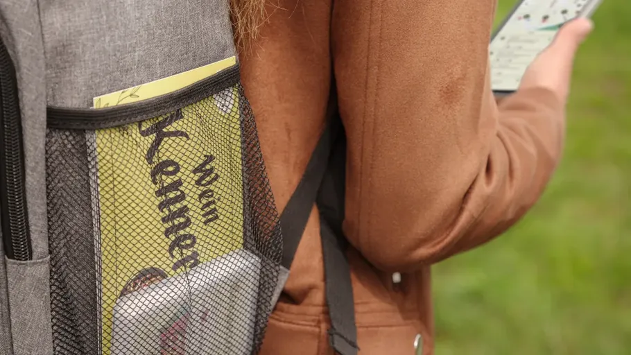 Person mit Rucksack, draußen am Handy.