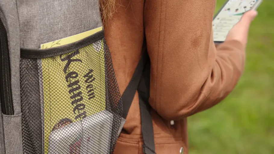 Rucksack mit Magazin, Person hält Handy draußen.