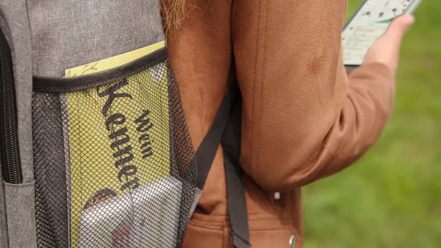 Person hält Handy mit Rucksack im Freien.