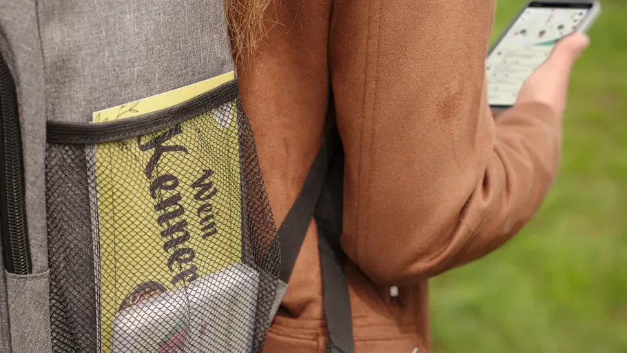 Person holds phone next to backpack outdoors.