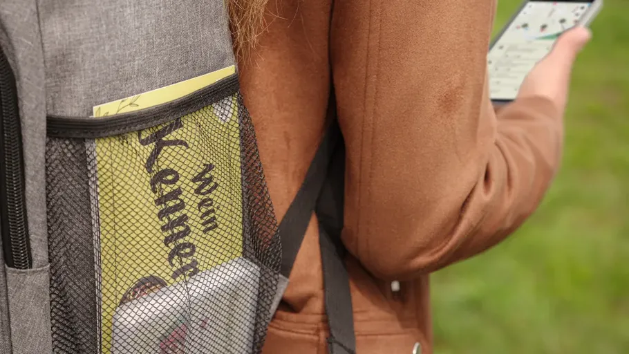 Person with backpack holding smartphone outdoors.