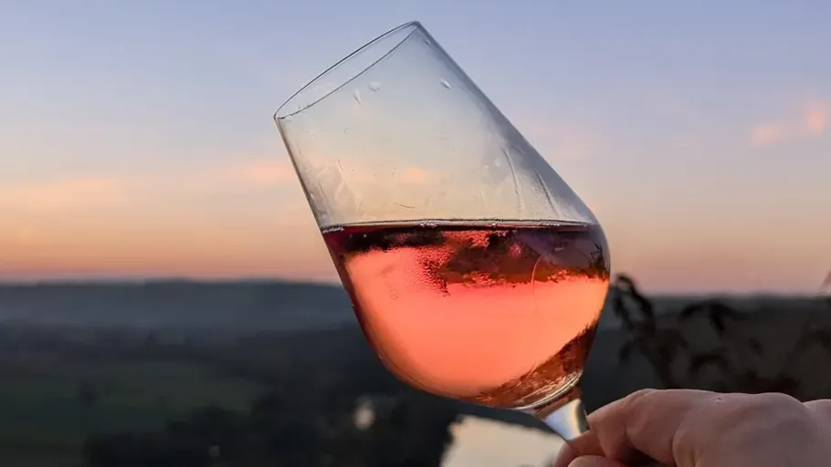 Weinglas gegen Sonnenuntergangshimmel erhoben.