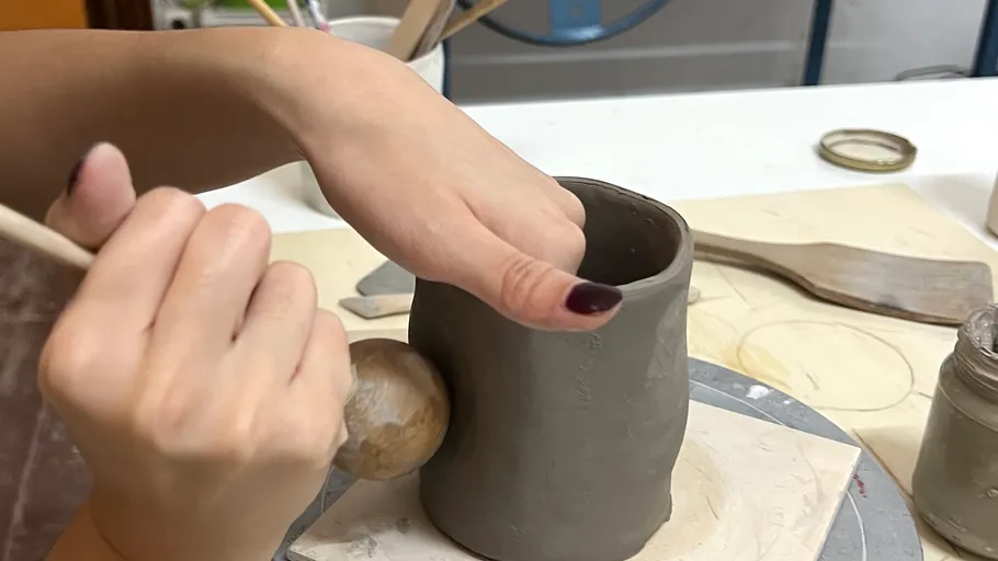 Hands sculpting clay mug on table.