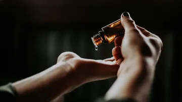 Hands pouring oil from small bottle indoors.