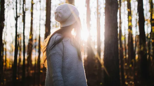 Woman in woods, sunlight through trees.