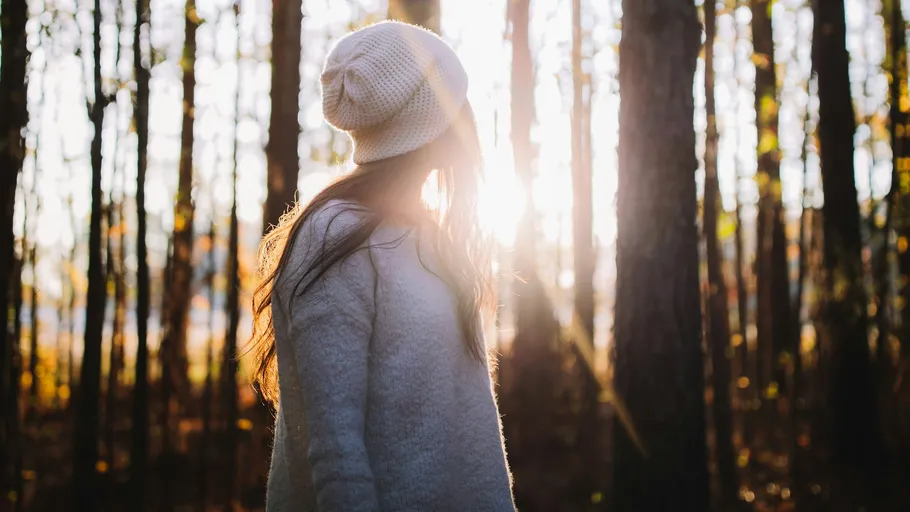 Woman in woods, sunlight through trees.