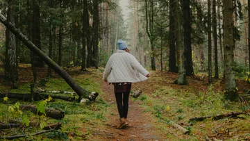 Person walking in forest wearing white jacket.