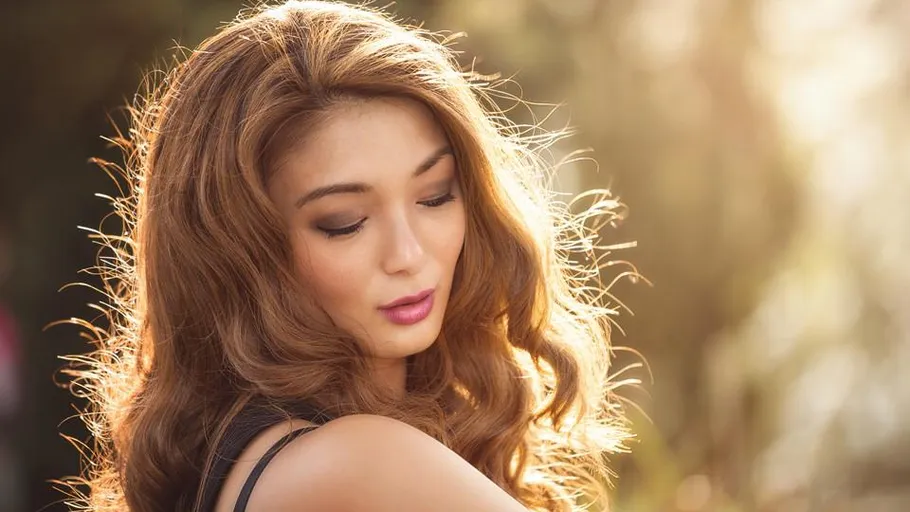 Woman with long hair in sunlight, eyes closed.