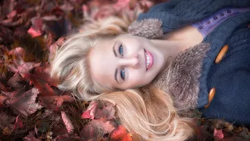 Woman lying in autumn leaves smiling.