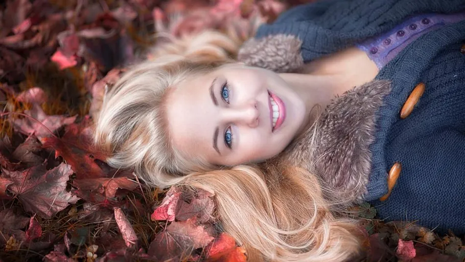 Woman lying in autumn leaves smiling.
