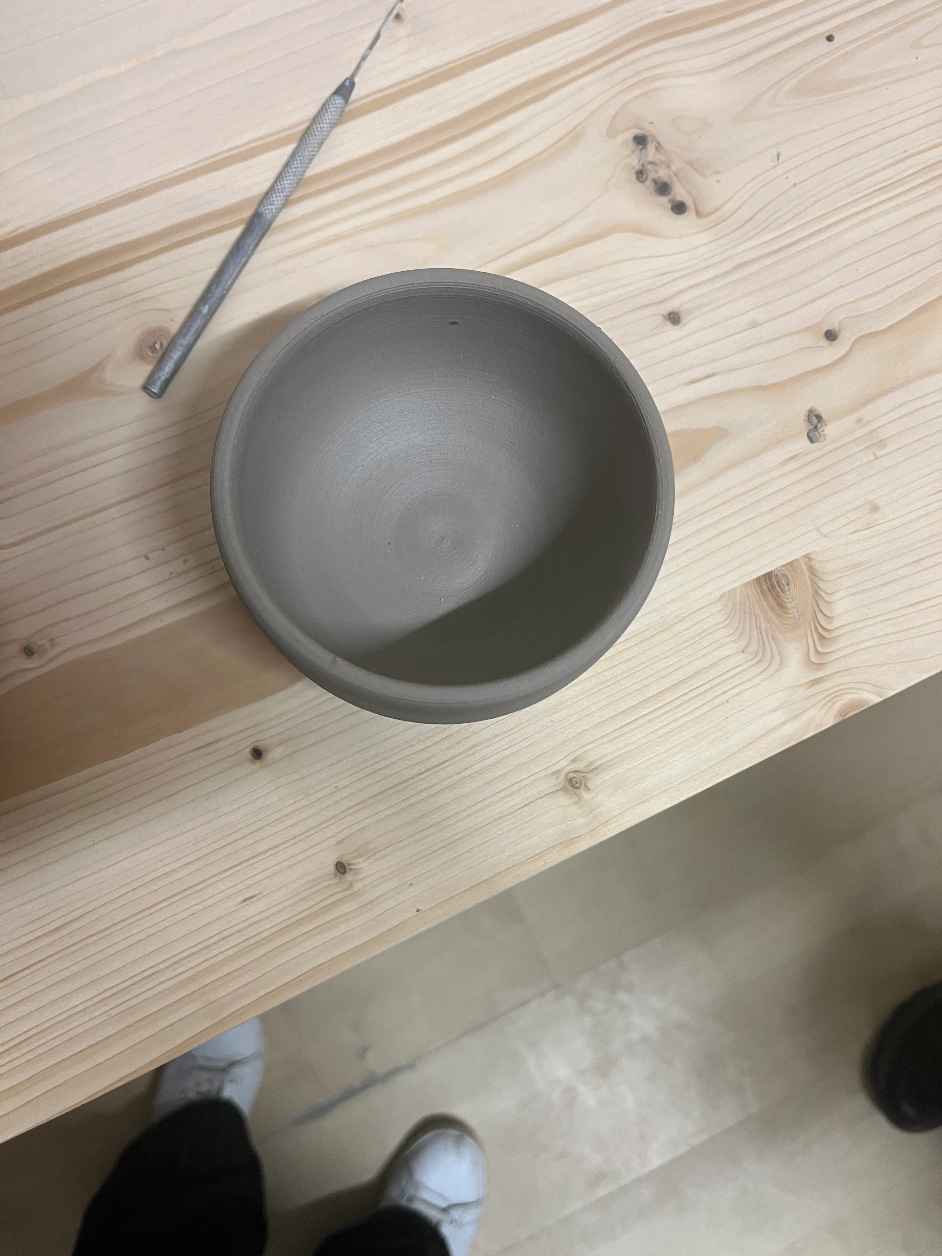 Tonschale auf Holztisch mit Werkzeug.