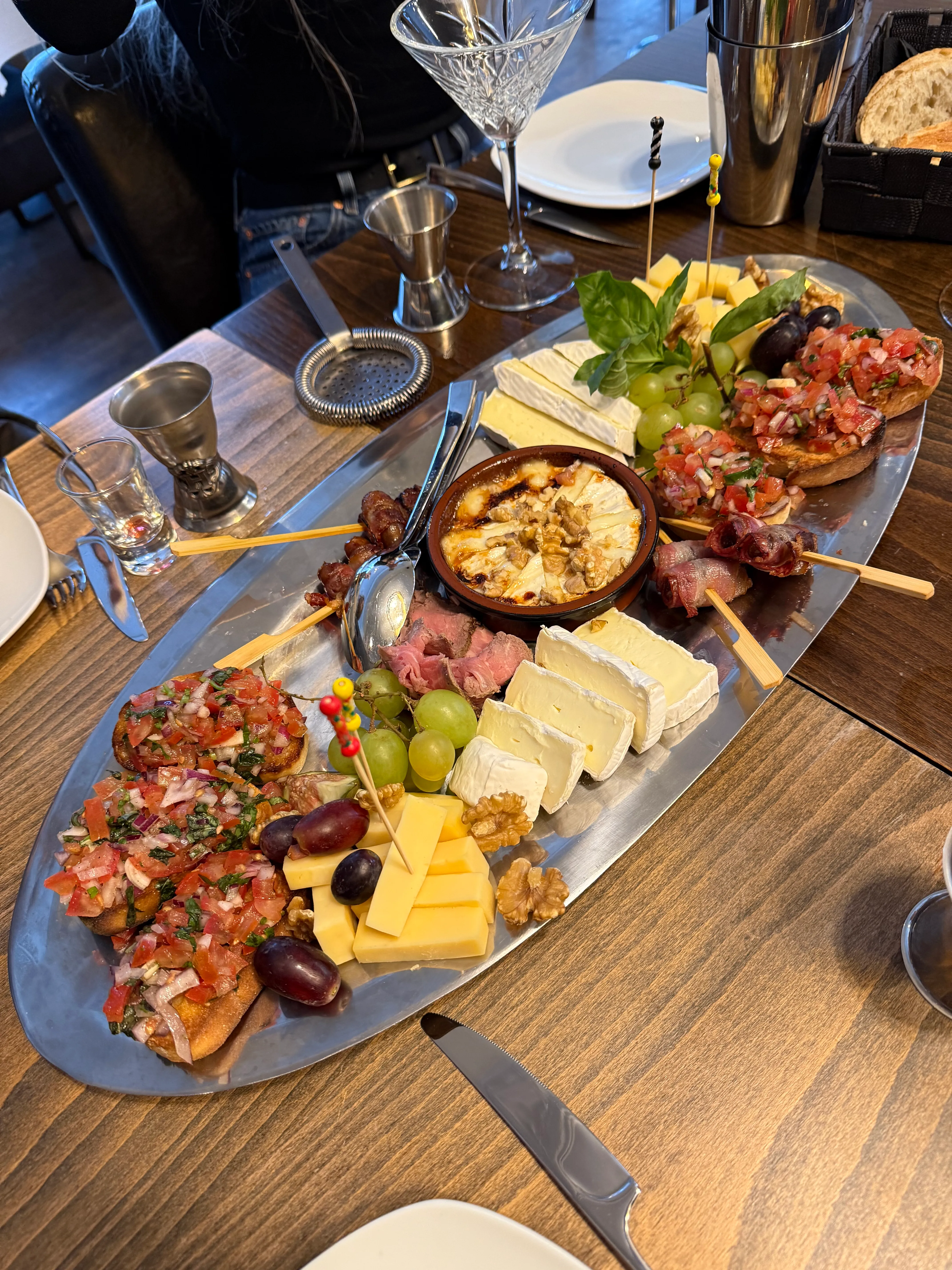 Platte mit Käse, Bruschetta und Beilagen auf Tisch.