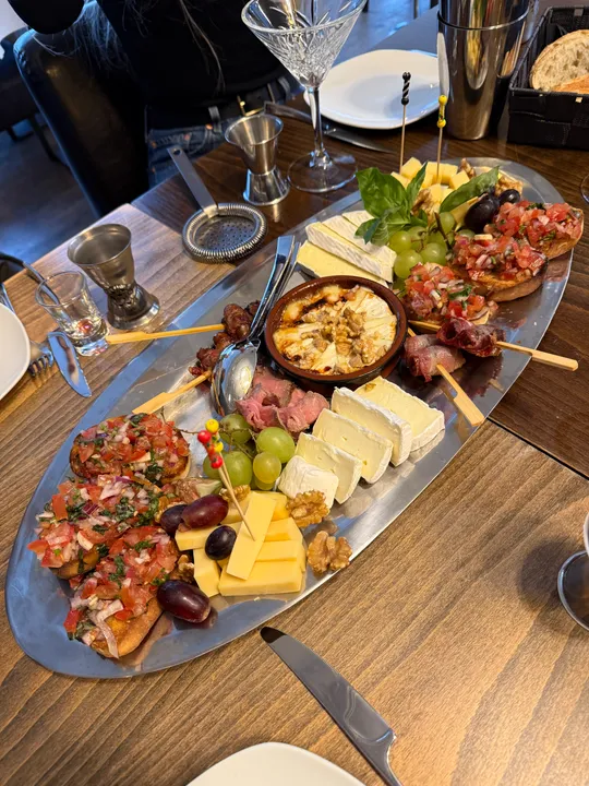 Platte mit Käse, Bruschetta und Beilagen auf Tisch.