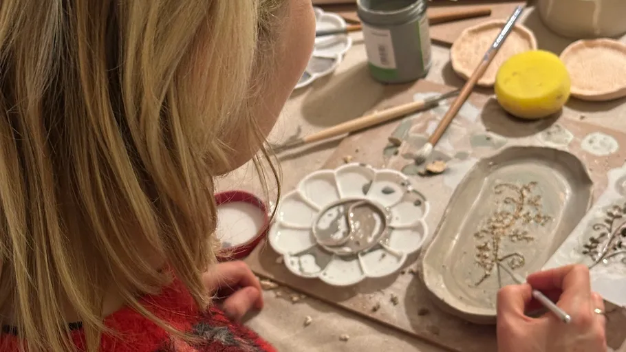 Person painting pottery on a table.