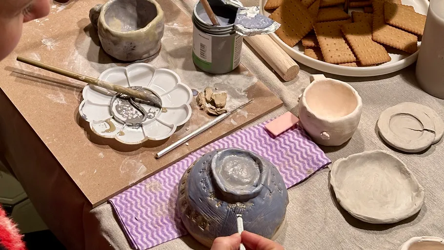 Person decorating pottery with tools on table.